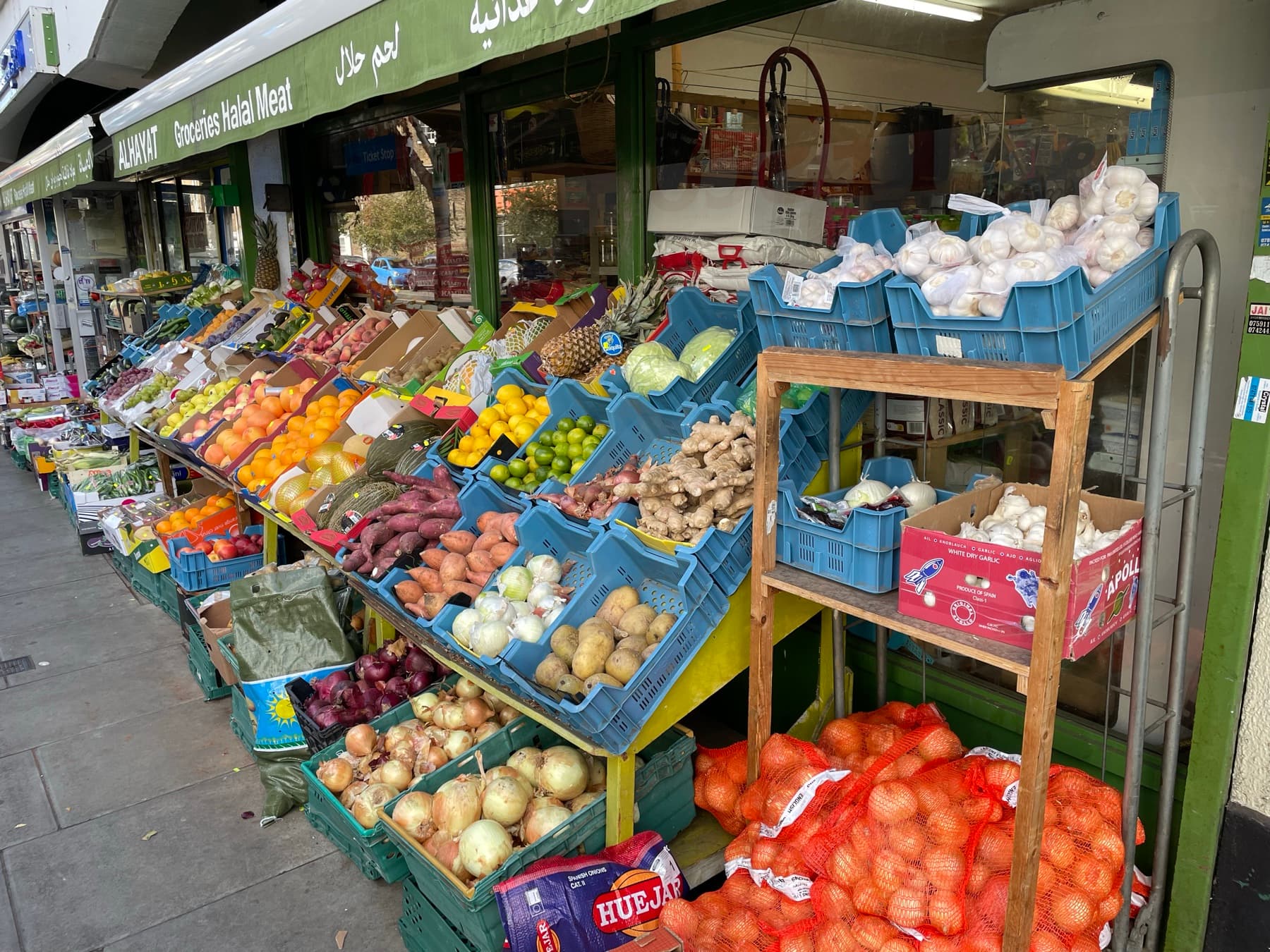 The Alhayat shopfront on Lupus Street, blue ALHAYAT lettering in English and Arabic above the green Groceries Halal Meat awning, with produce set out beneath it